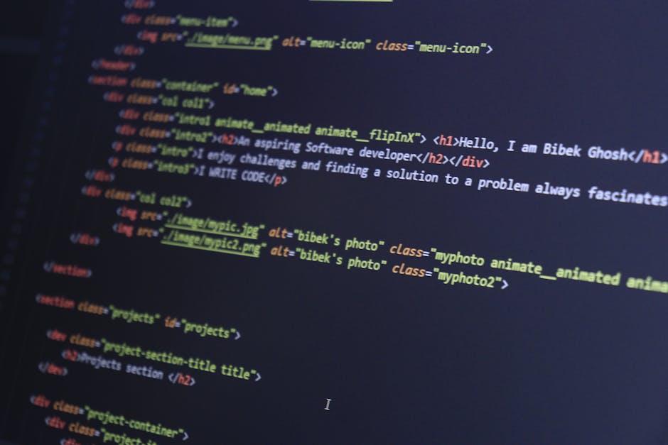 A person using a laptop computer on a dark surface indoors, with the screen displaying lines of code in various colors on a dark background. The individual's hands are positioned on the keyboard, with
